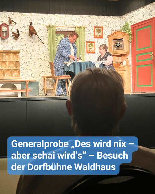 Eine ältere Person sitzt im Publikum und blickt auf eine kleine Theaterbühne. Dort spielen ein Schauspieler und eine Schauspielerin, sie sind gerade im Esszimmer am Tisch. Bildbeschriftung: Generalprobe „Des wird nix – aber schai wird’s“ – Besuch der Dorfbühne Waidhaus